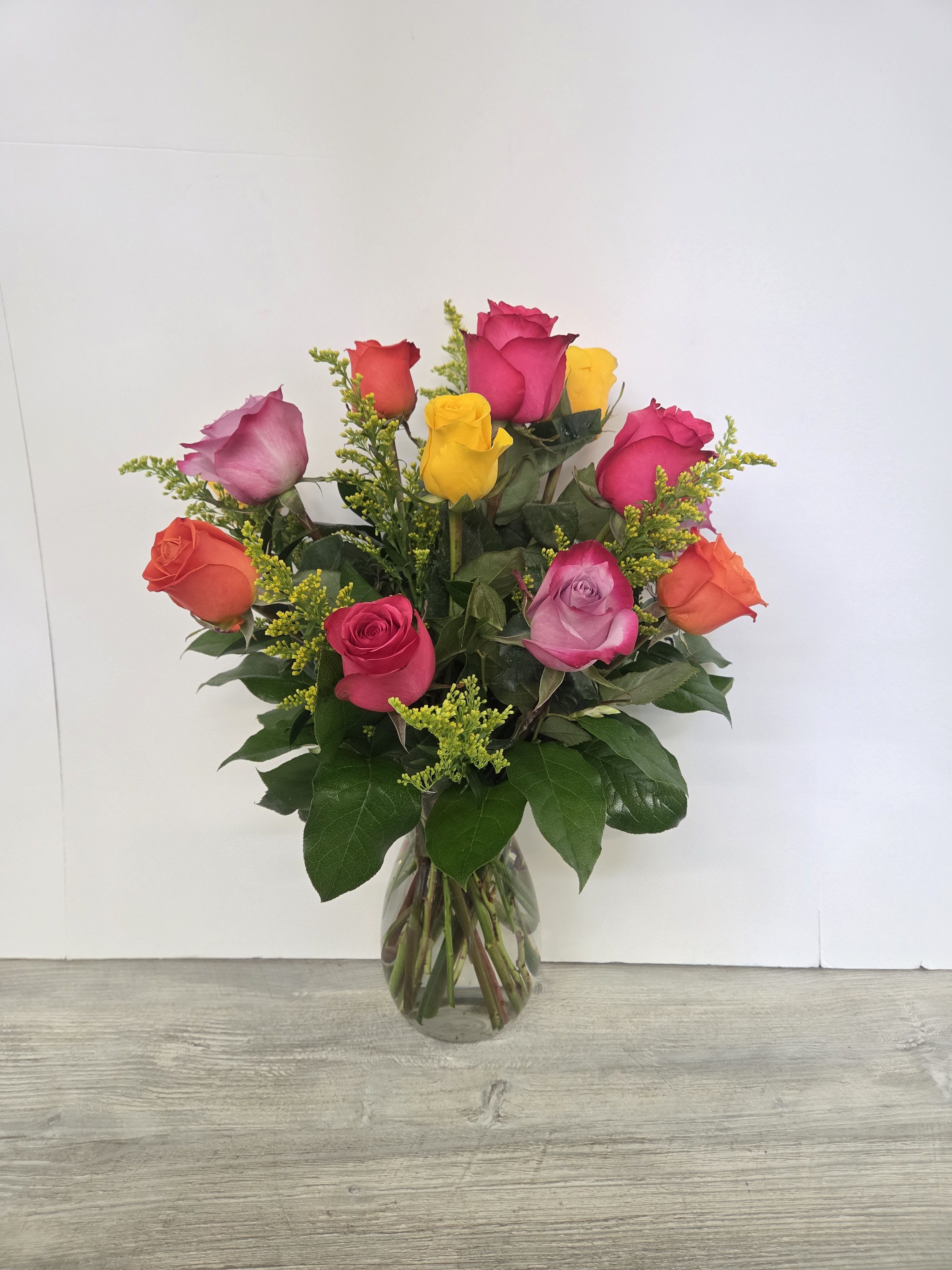 Glass vase of mixed pink, yellow, orange, and lavender roses with yellow filler flowers