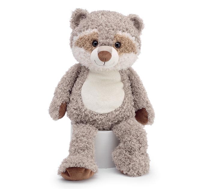Soft raccoon stuffed animal sitting upright on a small white cylinder