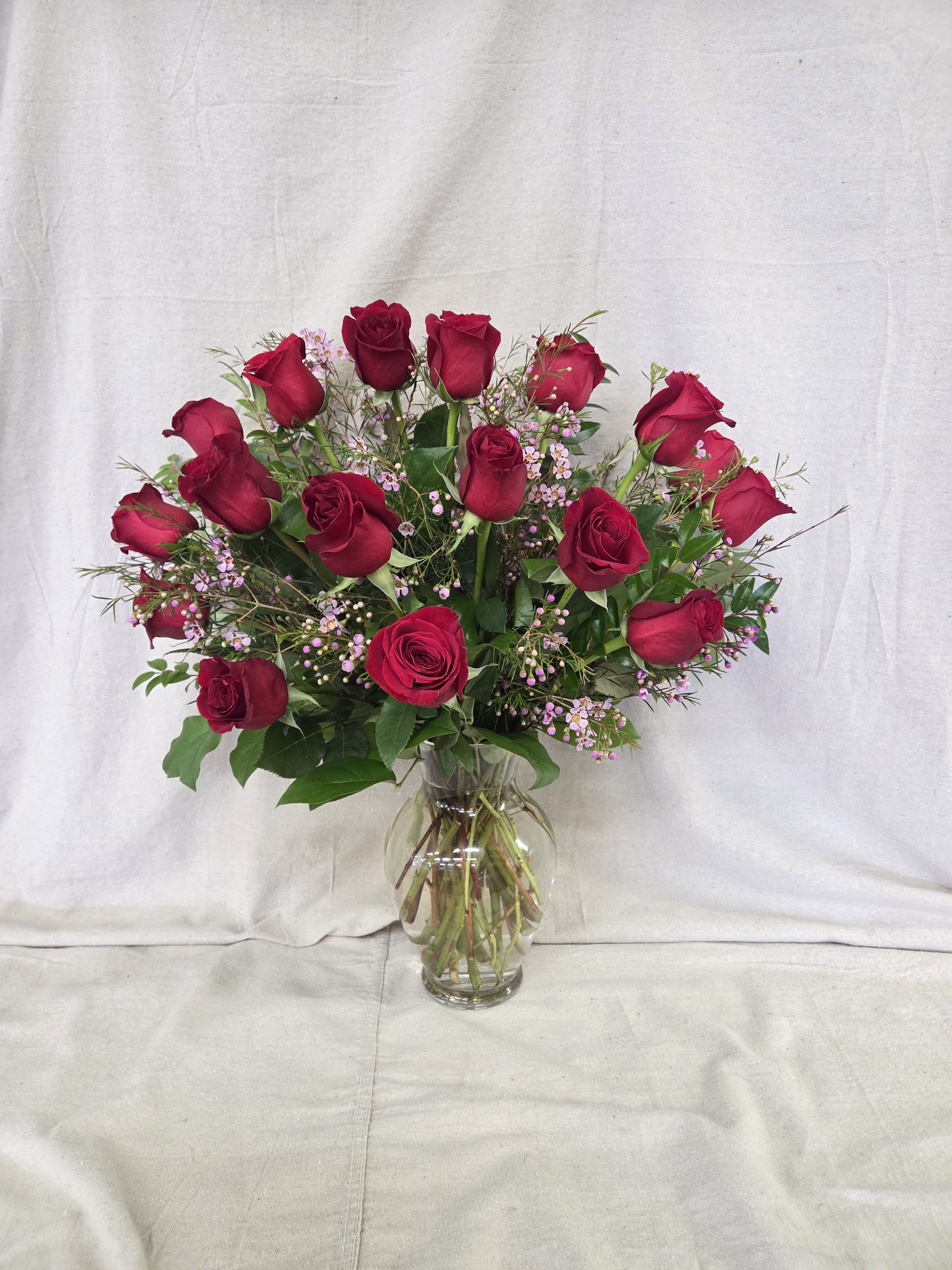 Tall arrangement of red roses with tiny pink blooms in a clear glass vase
