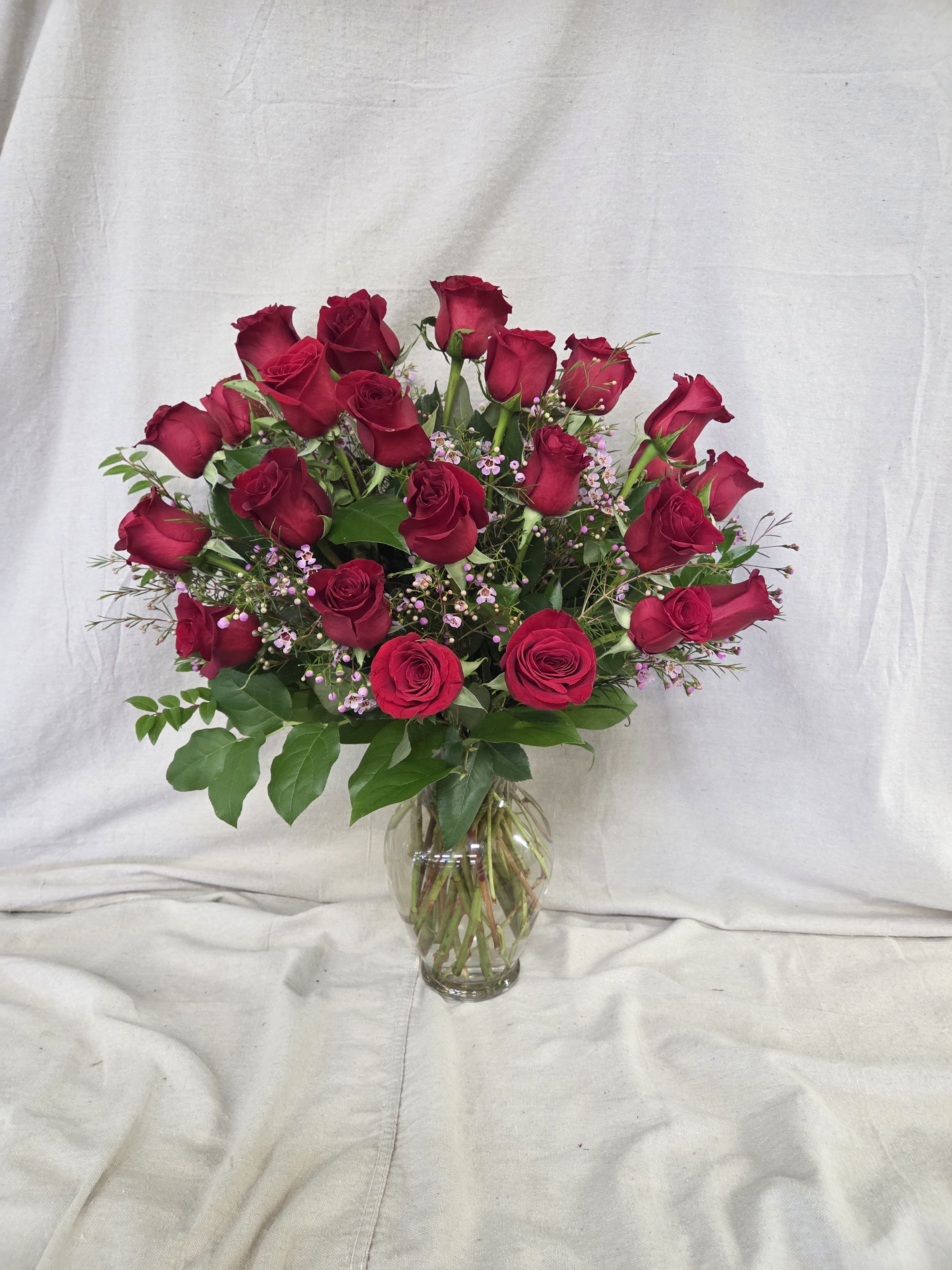 Tall arrangement of long-stem red roses with small pink filler flowers in a clear glass vase