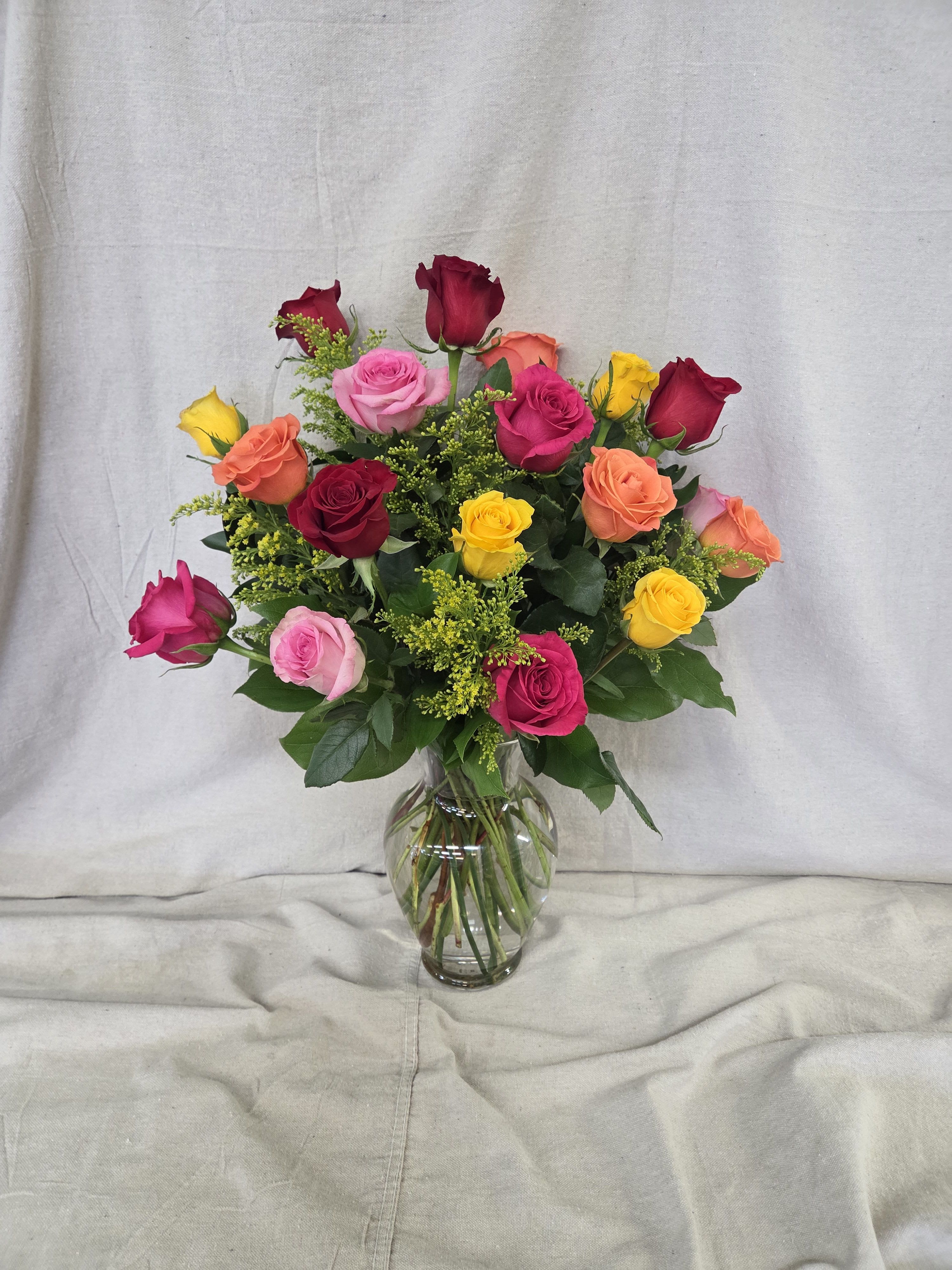 Mixed bouquet of colorful roses arranged in a clear glass vase.