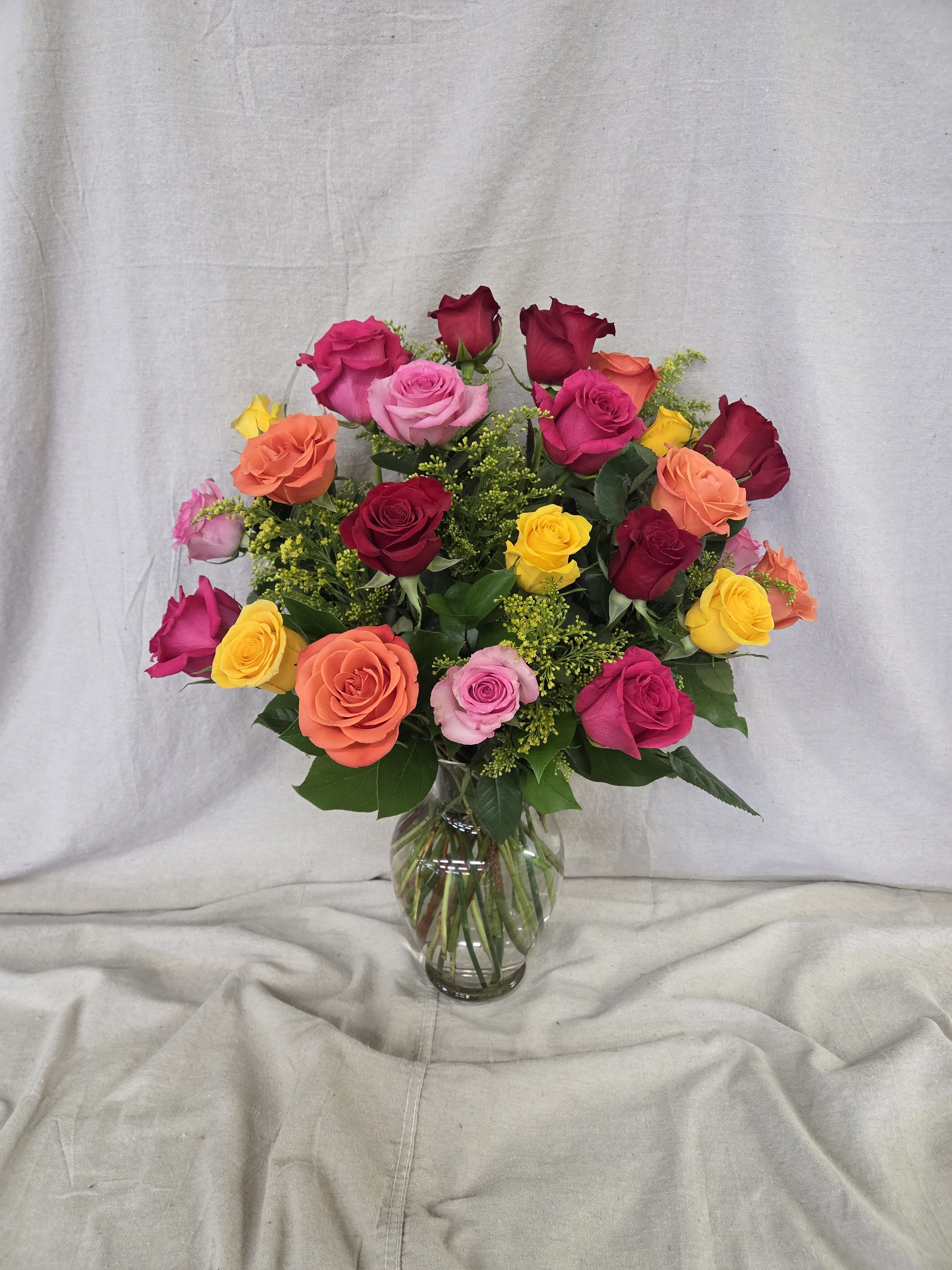 Mixed bouquet of bright roses in pink, orange, yellow, and red arranged in a clear glass vase
