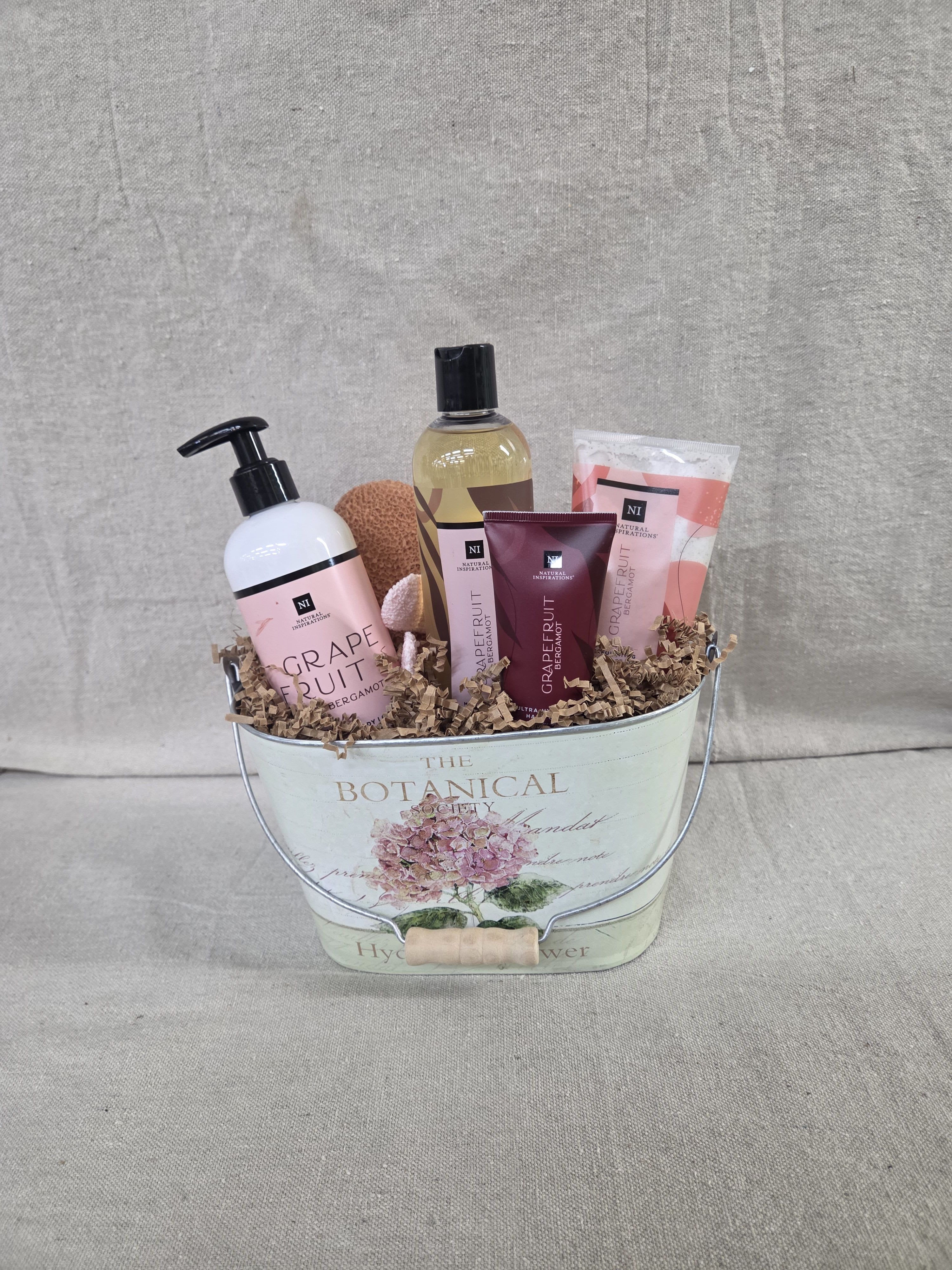 Grapefruit-scented bath gift set arranged in a floral metal pail with crinkle paper filler