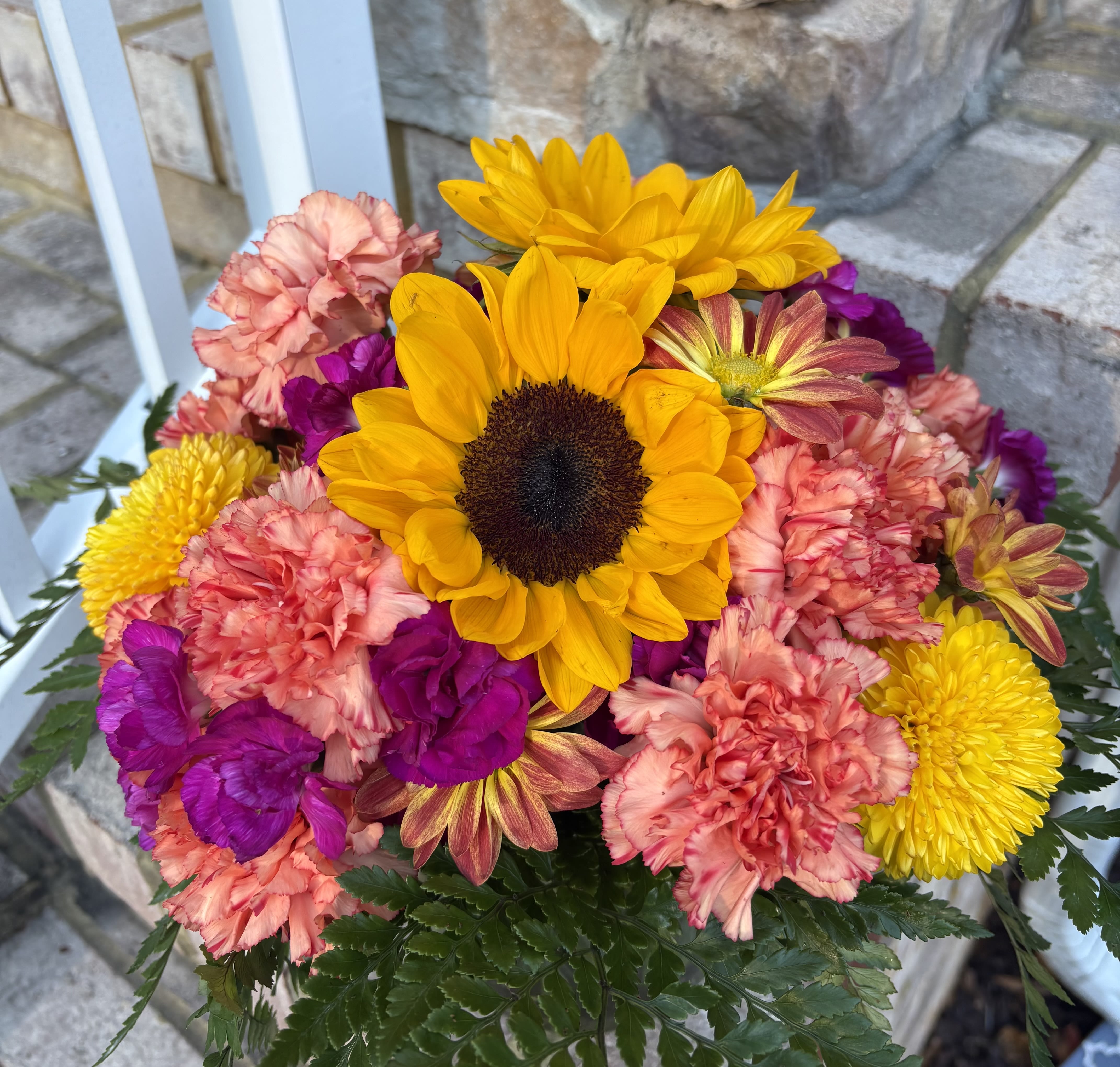 Starburst - Bursting with the vibrant colors of the season, the Starburst arrangement brings warmth and cheer to any space. Featuring golden sunflowers, vivid purple blooms, sunny yellow mums, and peachy-orange carnations, this joyful mix captures the beauty of fall in full bloom. Perfect for brightening a home, celebrating a special day, or simply sending a little sunshine someone’s way.  Best For: Fall birthdays, thank-you gifts, or “just because” moments that deserve a little extra color.