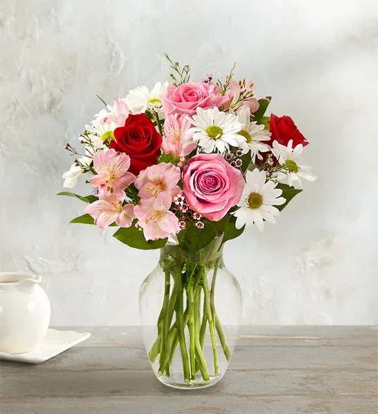 Pink and red roses with white daisies in a clear glass vase