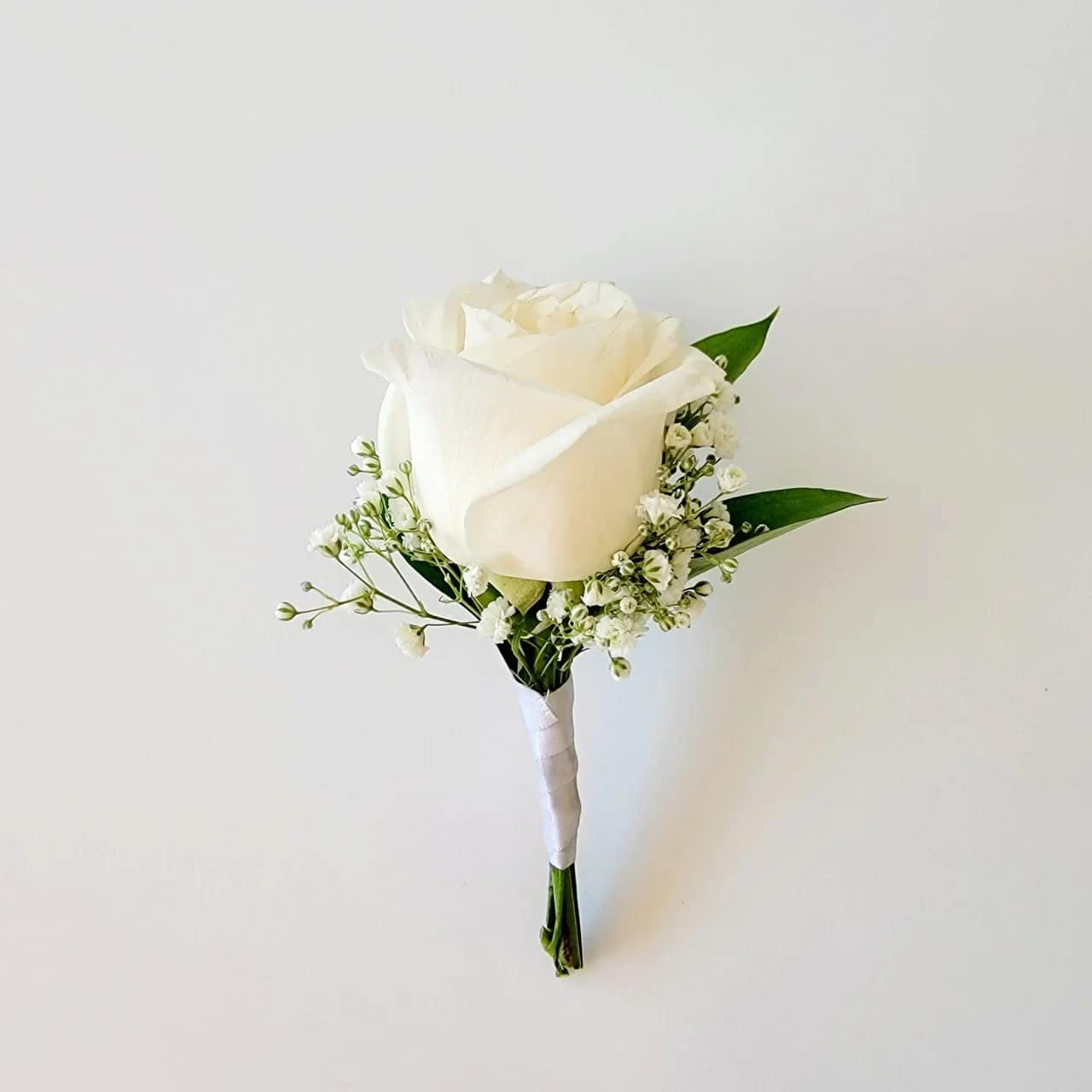 White rose boutonniere with baby's breath and green leaves