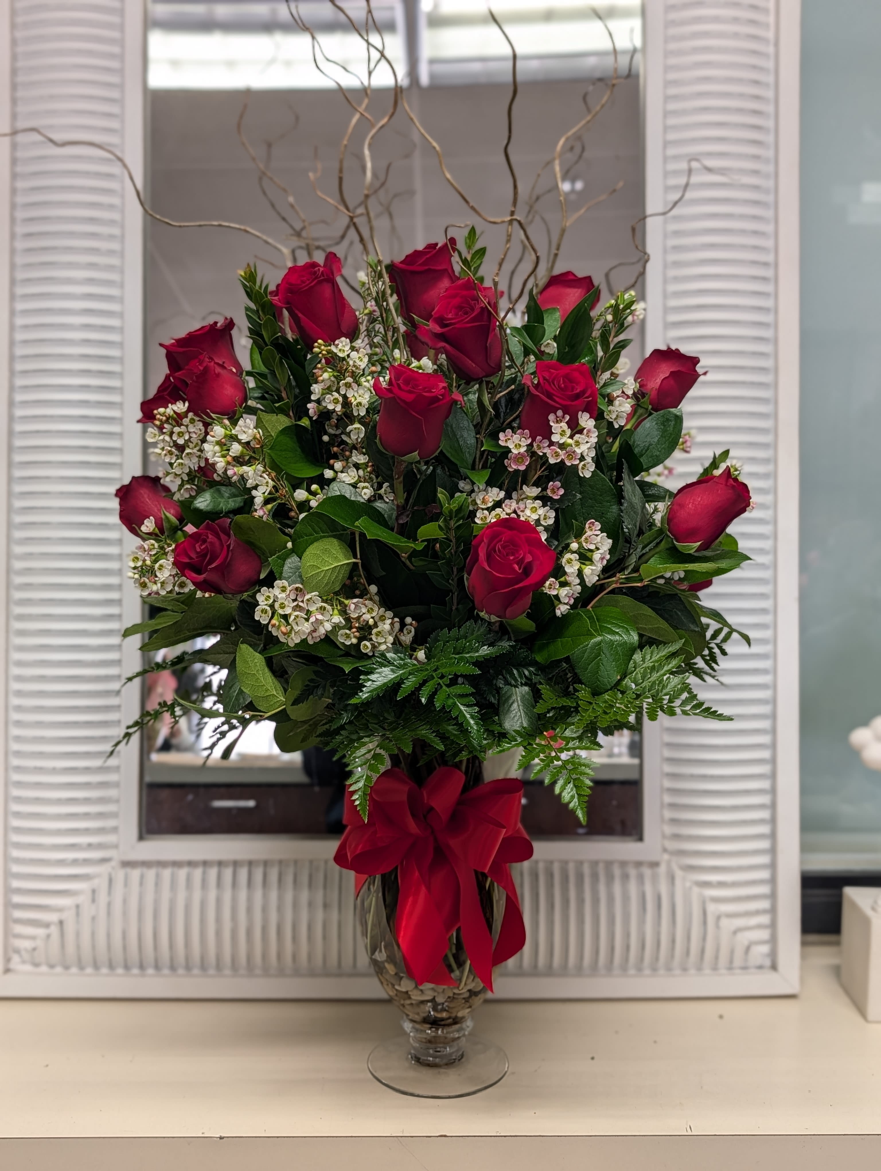 Red rose arrangement in a glass vase with a red ribbon