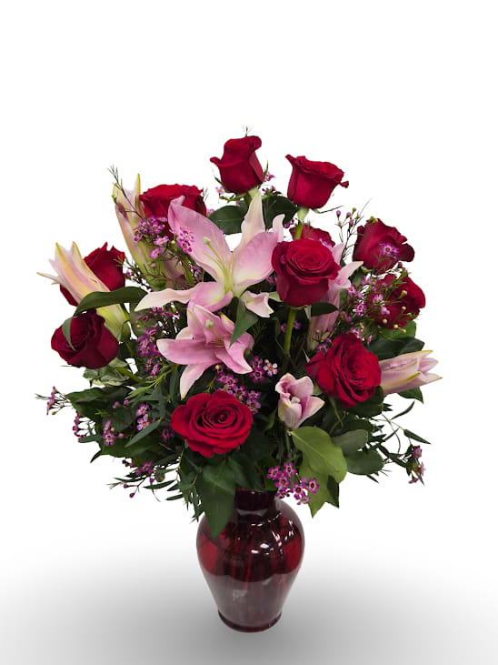 Red roses and pink lilies arranged in a red glass vase