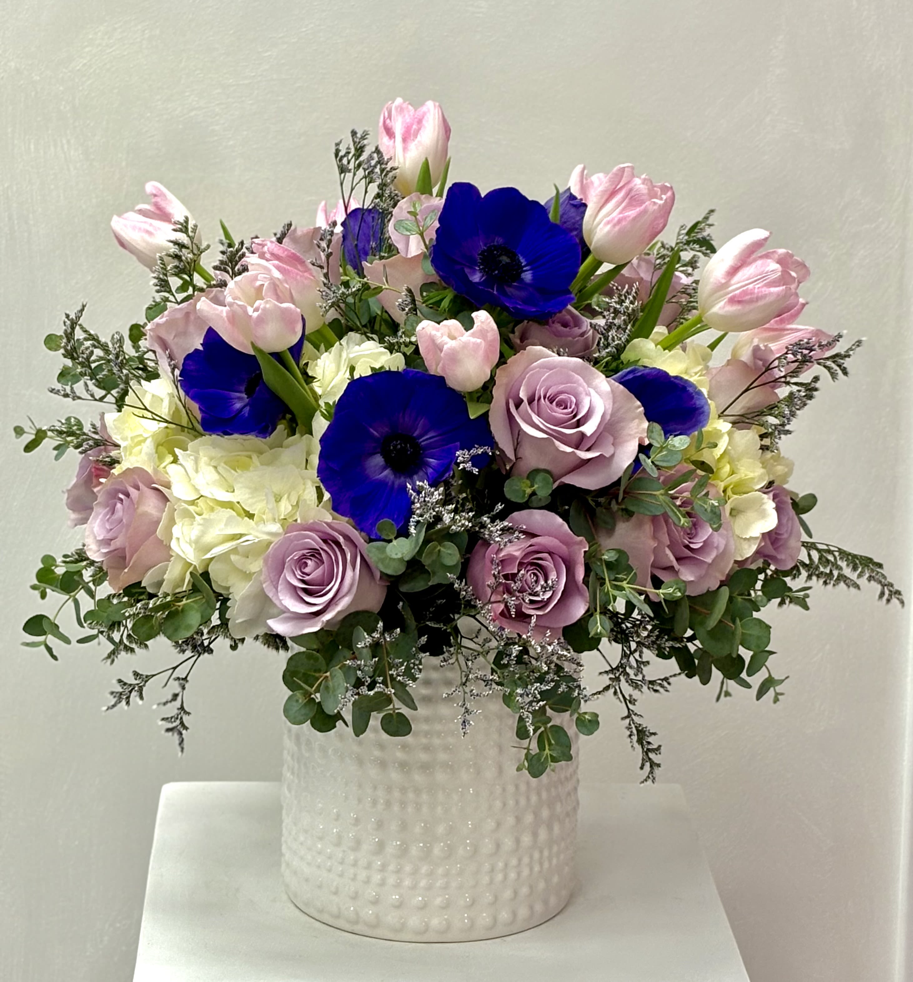 Pink tulips, lavender roses, and blue anemones in a white vase