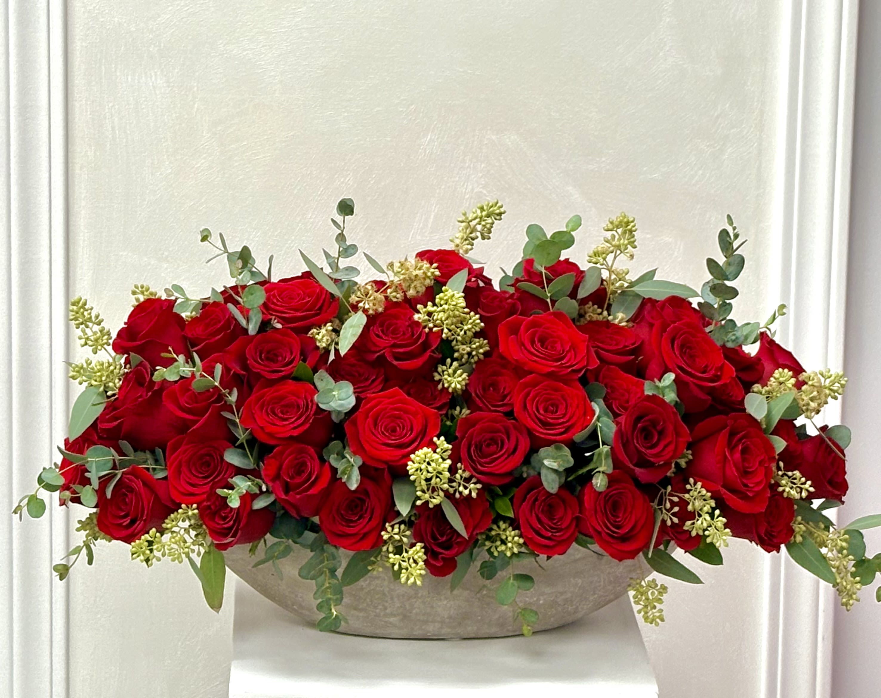 Low arrangement of red roses in a shallow bowl with eucalyptus accents