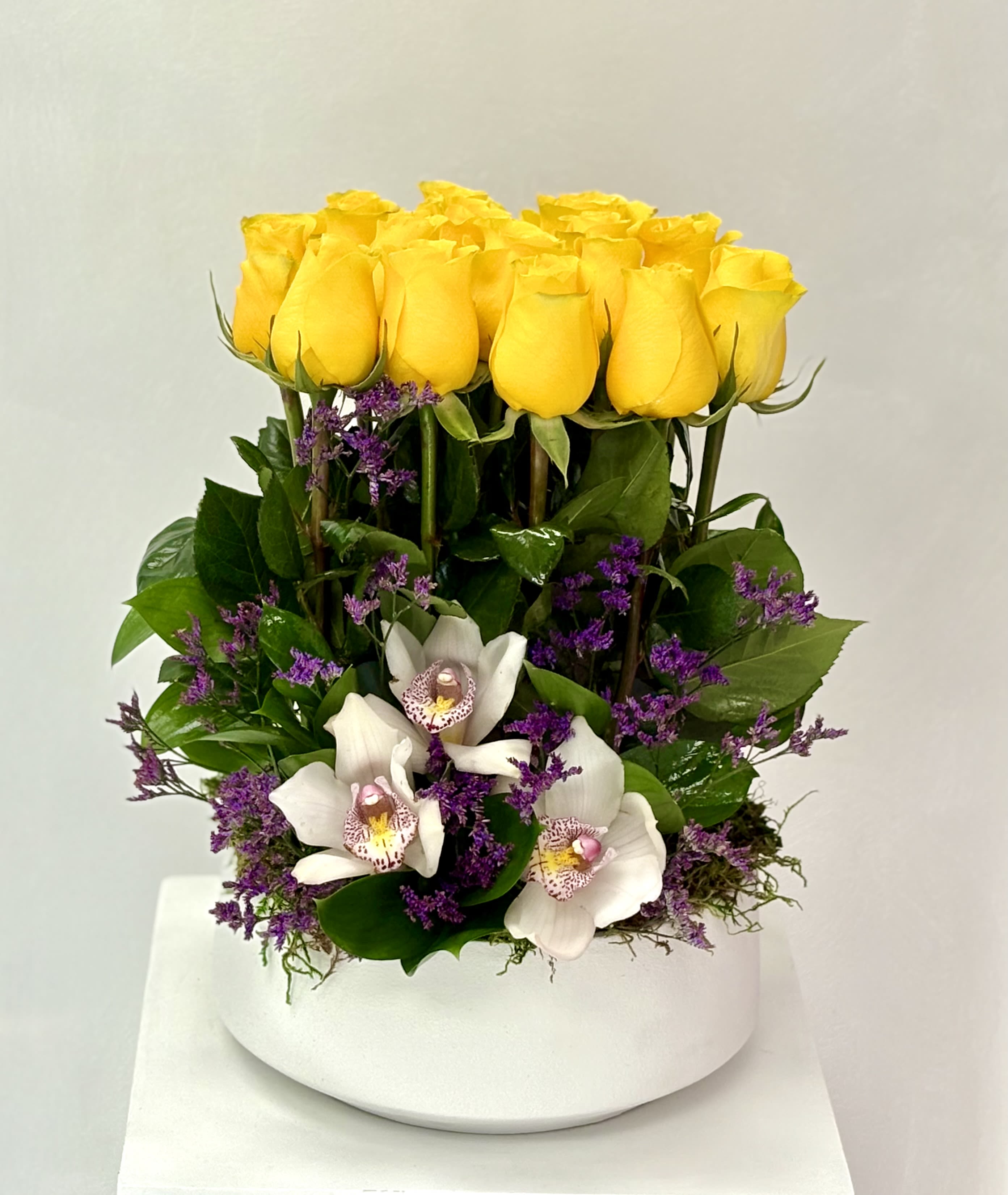Yellow roses and white orchids arranged in a white vase