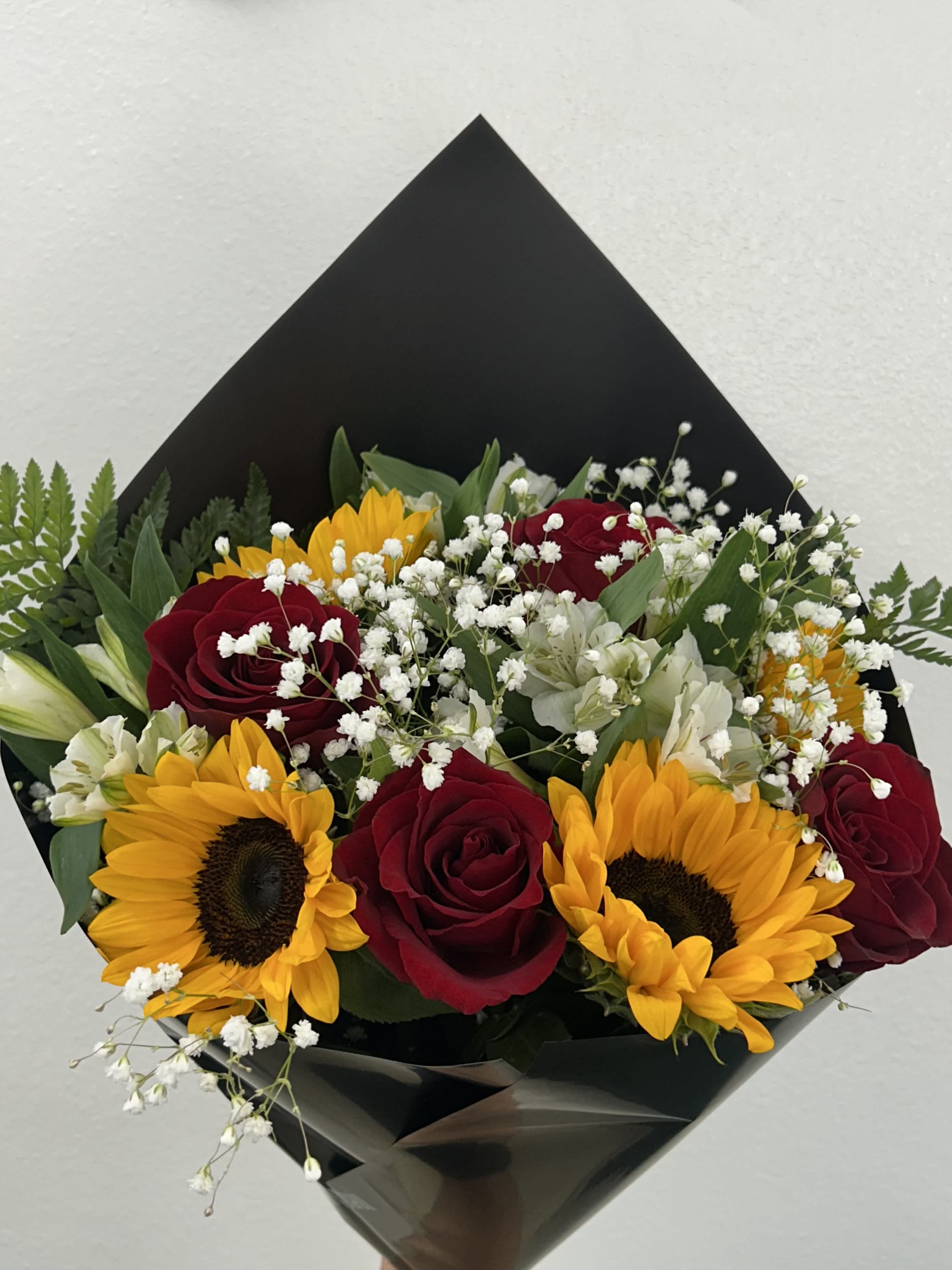 Bouquet of red roses and sunflowers with white filler flowers in black wrap