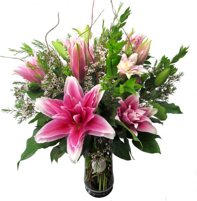 Pink lilies in a glass vase with mixed greenery