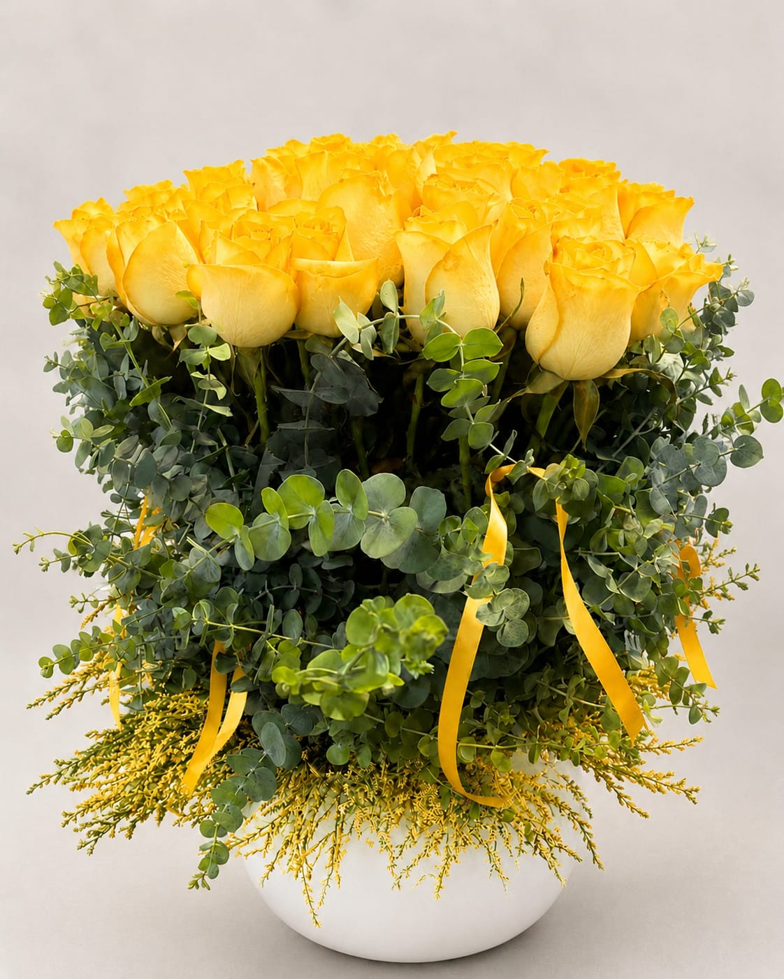 Yellow roses in a white vase with eucalyptus and yellow ribbon