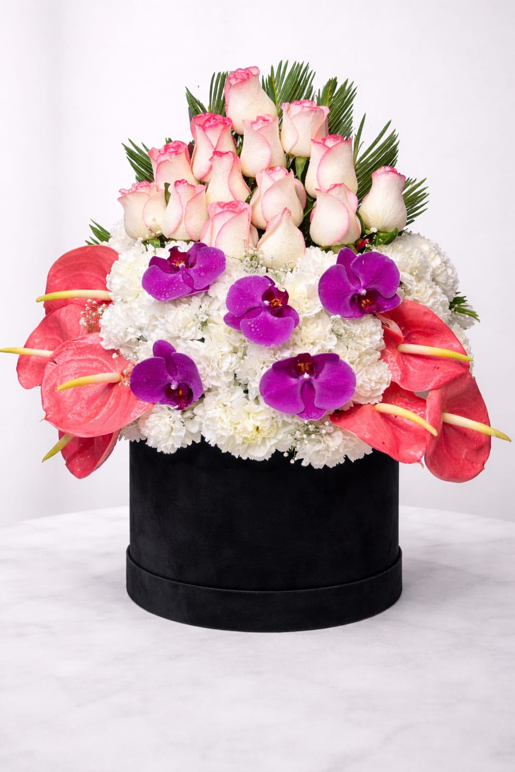 Pink-tipped roses, purple orchids, and white flowers in a black hat box