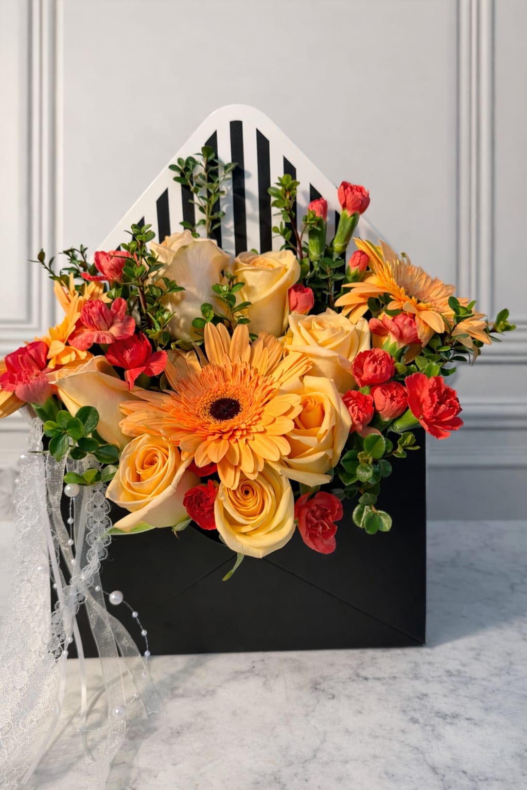 Bouquet of yellow roses, orange gerbera daisies, and red carnations in a black gift box