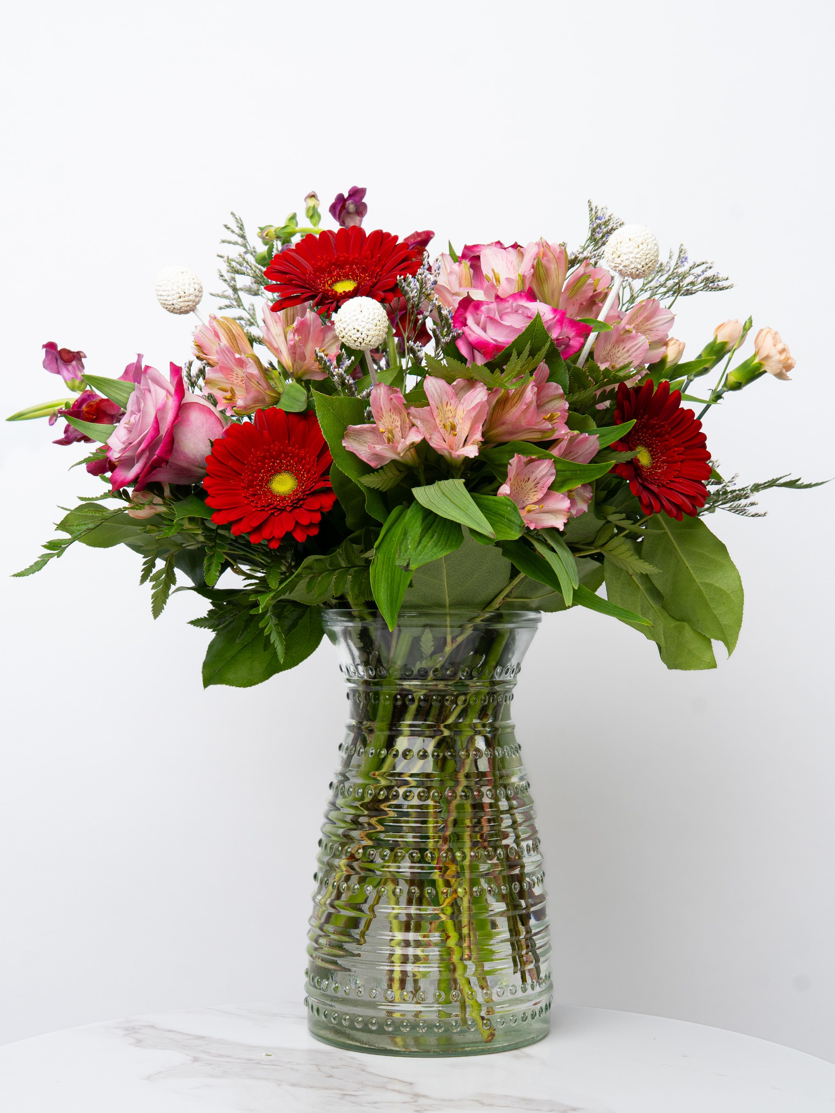 Bouquet of red gerbera daisies and pink flowers in a glass vase