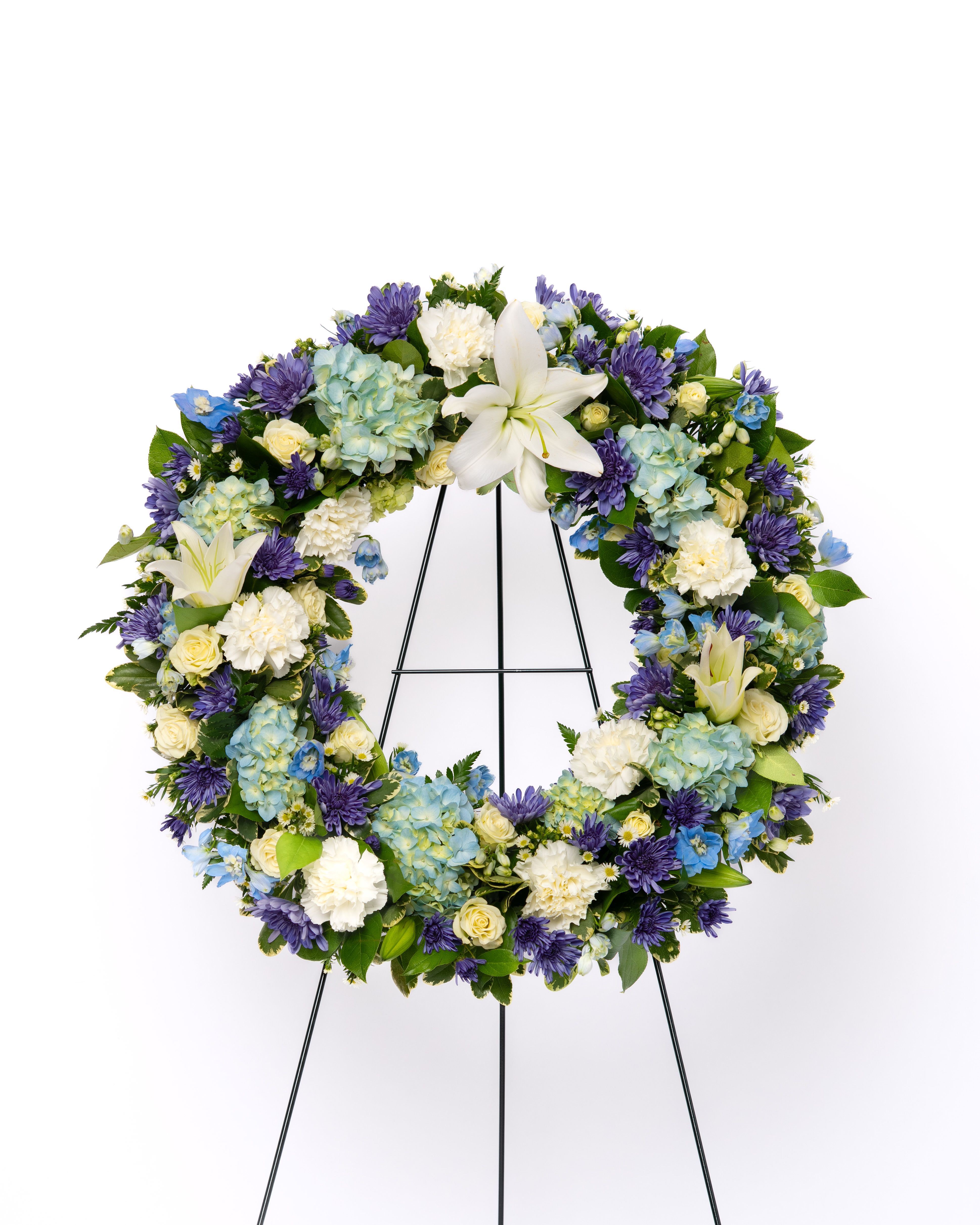 Our Gentle Thoughts Collection: 18" Open Wreath of White &amp; Blue Blooms - A classic circular tribute symbolizing eternal life and remembrance, this wreath is designed in a serene palette of whites and blues. The combination offers a sense of peace, calm, and reflection, making it a refined and respectful expression of sympathy. Its balanced, full shape creates a beautiful and composed presence at any service.  Each arrangement is thoughtfully designed using the freshest blooms available. Flower varieties may vary based on availability while maintaining the overall style, color palette, and value.  Approximate Dimensions of Floral Tribute: 48" tall x 25" wide  Color &amp; Customization: Need a custom color scheme? Contact us for more information. Our most popular palettes include whites, whites and greens, whites and blues, pinks and whites, pastel shades, and colorful designs.  Delivery: All sympathy pieces are hand-delivered by the Schultz Floral team.