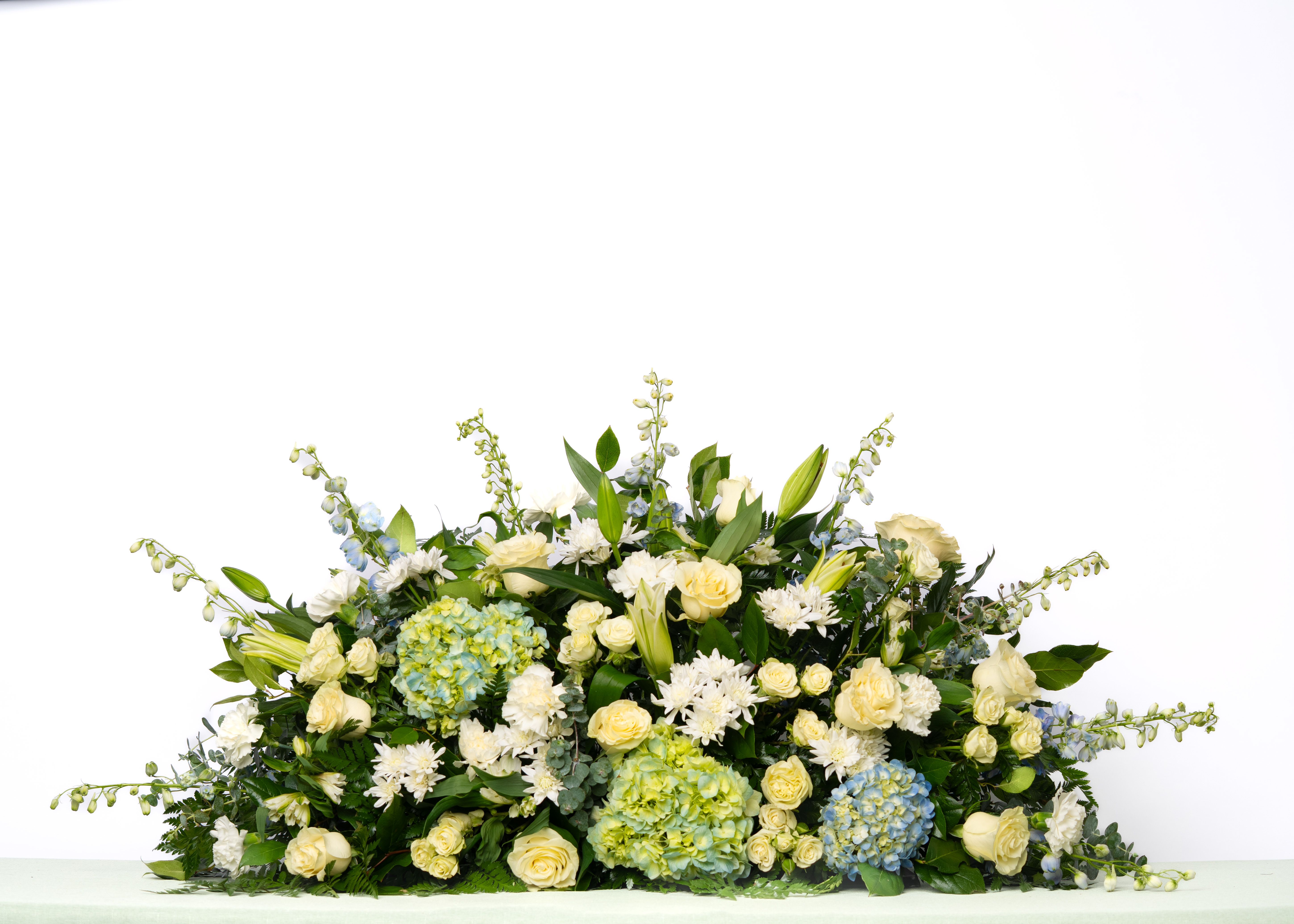 Our Gentle Thoughts Collection: Full Casket Spray in White and Blue - A refined combination of white and blue florals creates a peaceful and elegant tribute. Designed to honor and reflect with calm, timeless beauty.  Each arrangement is thoughtfully designed using the freshest blooms available. Flower varieties may vary based on availability while maintaining the overall style, color palette, and value.  Approximate Dimensions of Floral Tribute: 20" tall x 48" wide  Color &amp; Customization: Need a custom color scheme? Contact us for more information. Our most popular palettes include whites, whites and greens, whites and blues, pinks and whites, pastel shades, and colorful designs.  Delivery: All sympathy pieces are hand-delivered by the Schultz Floral team.