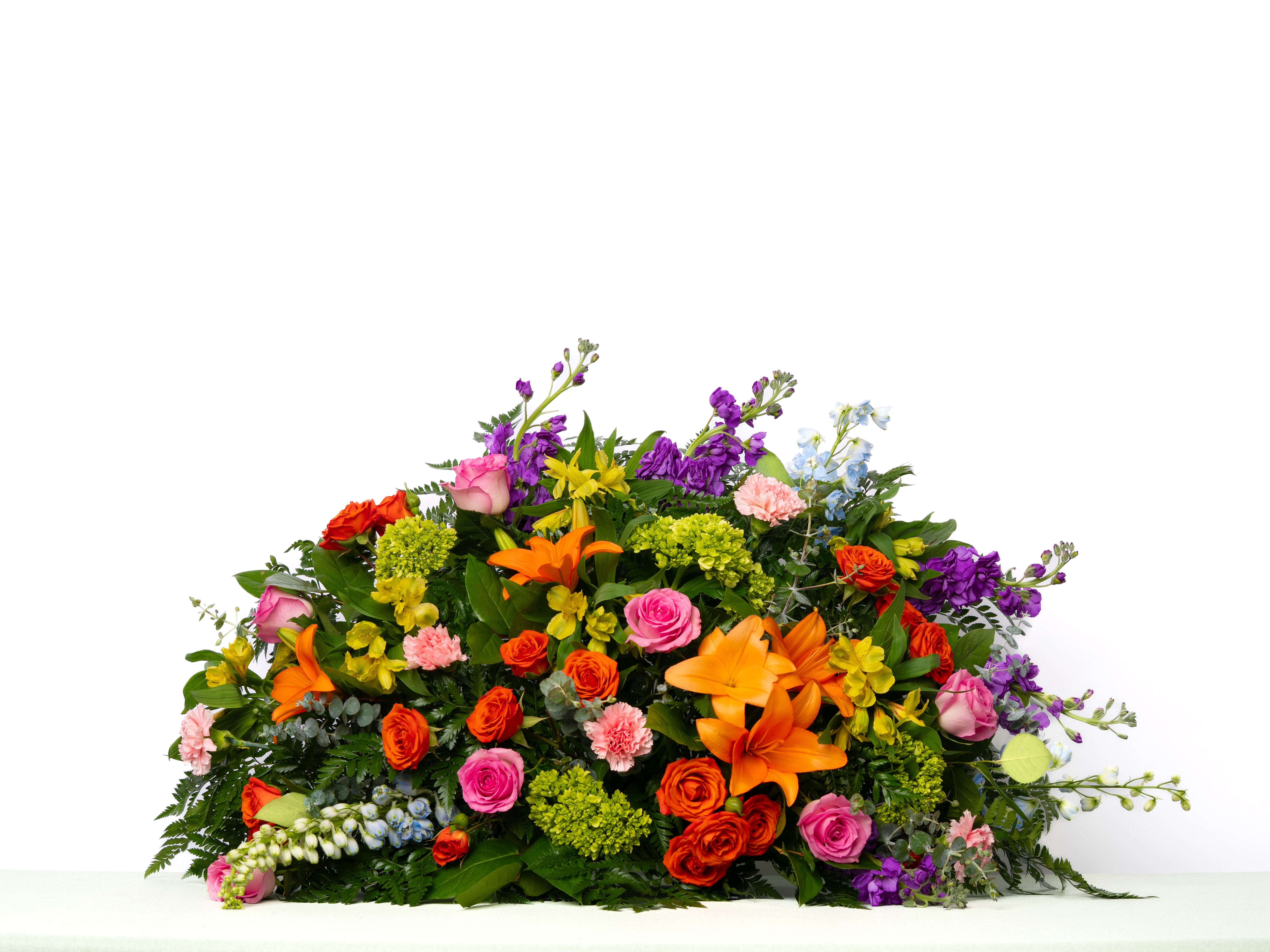 Our Bold Collection: Half Casket Spray in Colorful Blooms - Vibrant and expressive, this design celebrates a life full of personality and joy. A colorful mix of seasonal blooms creates a meaningful and uplifting tribute.  Each arrangement is thoughtfully designed using the freshest blooms available. Flower varieties may vary based on availability while maintaining the overall style, color palette, and value.  Approximate Dimensions of Floral Tribute: 20" tall x 36" wide  Color &amp; Customization: Need a custom color scheme? Contact us for more information. Our most popular palettes include whites, whites and greens, whites and blues, pinks and whites, pastel shades, and colorful designs.  Delivery: All sympathy pieces are hand-delivered by the Schultz Floral team.