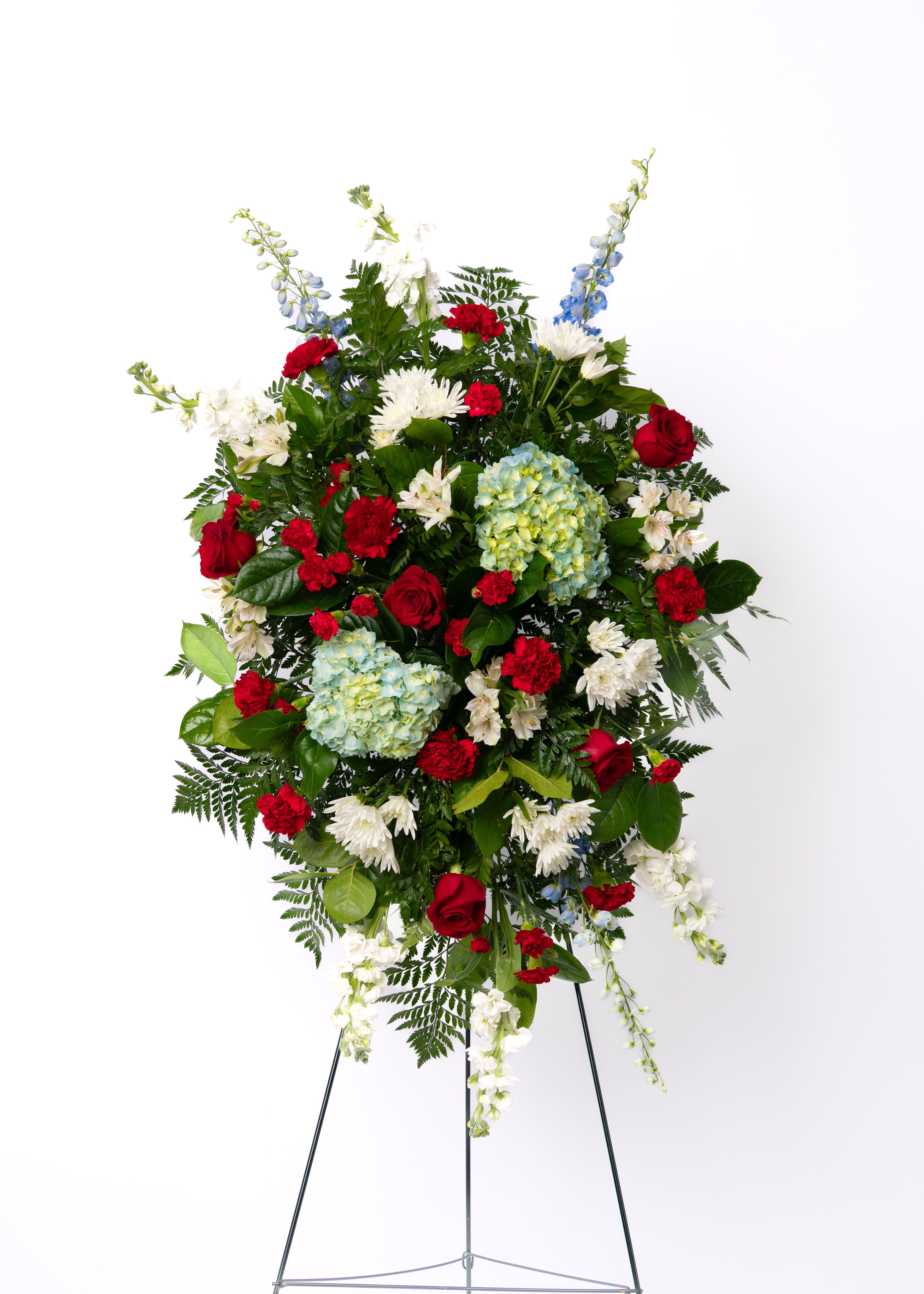 Tall red, white, and blue standing spray with roses, hydrangeas, and mums on a metal easel