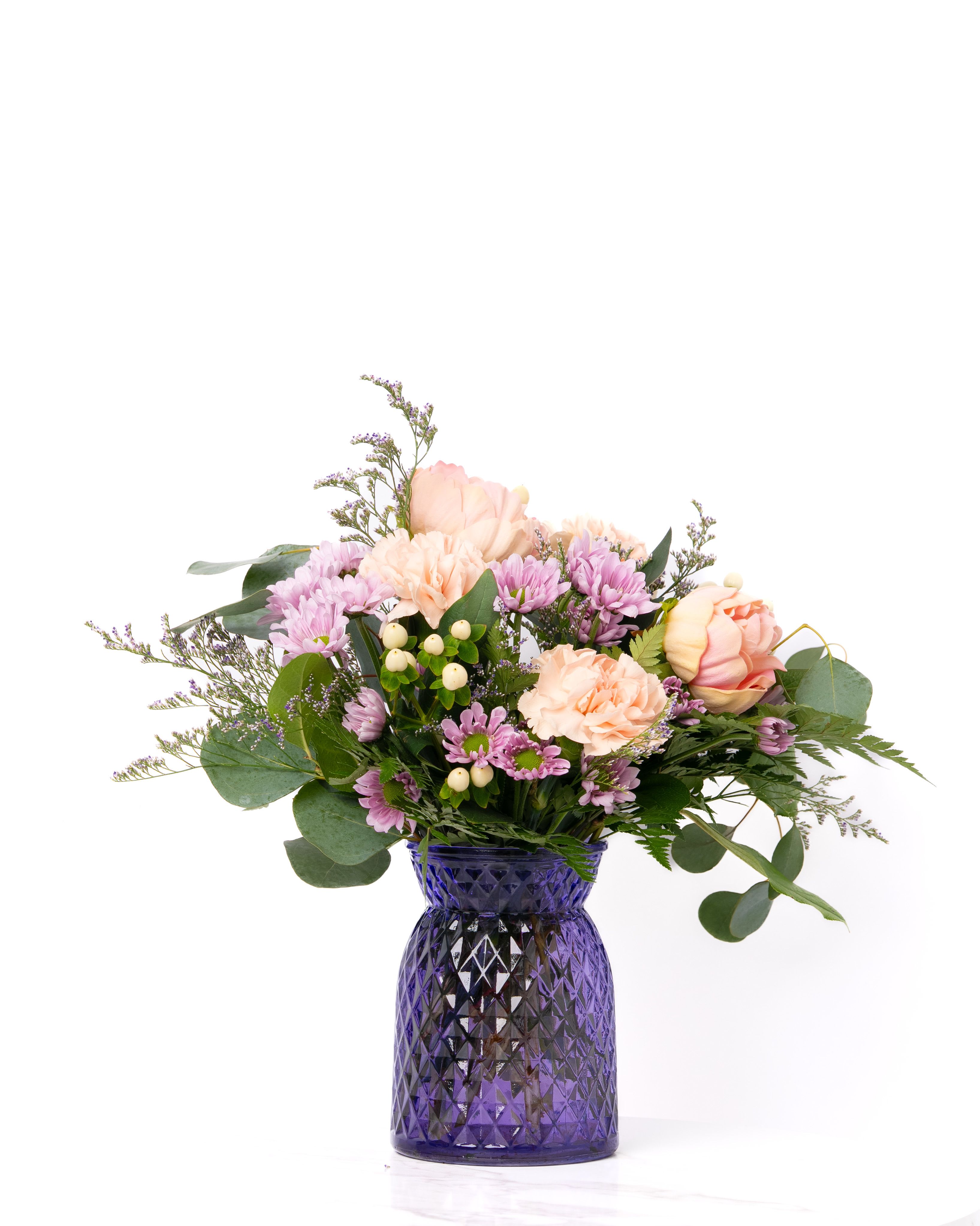 Mixed bouquet of peach roses and carnations with lavender mums in a purple glass vase