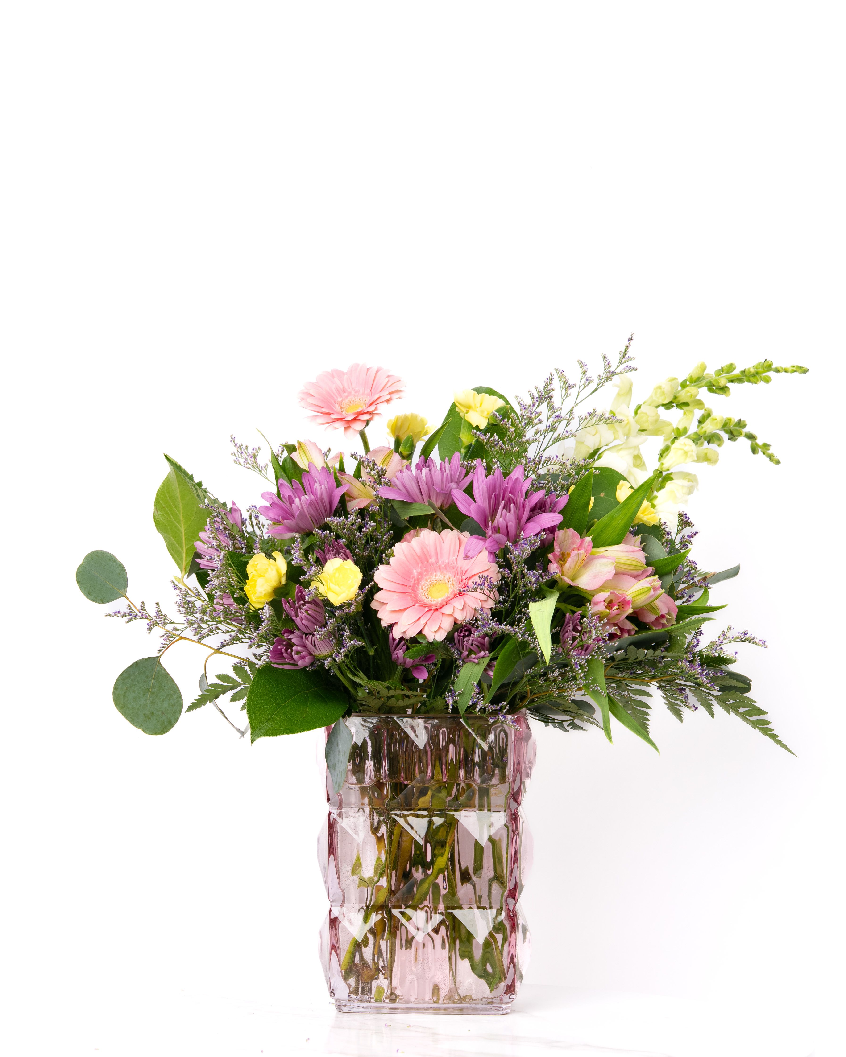 Mixed bouquet of pink gerbera daisies, purple mums, and yellow roses in a pink textured glass vase