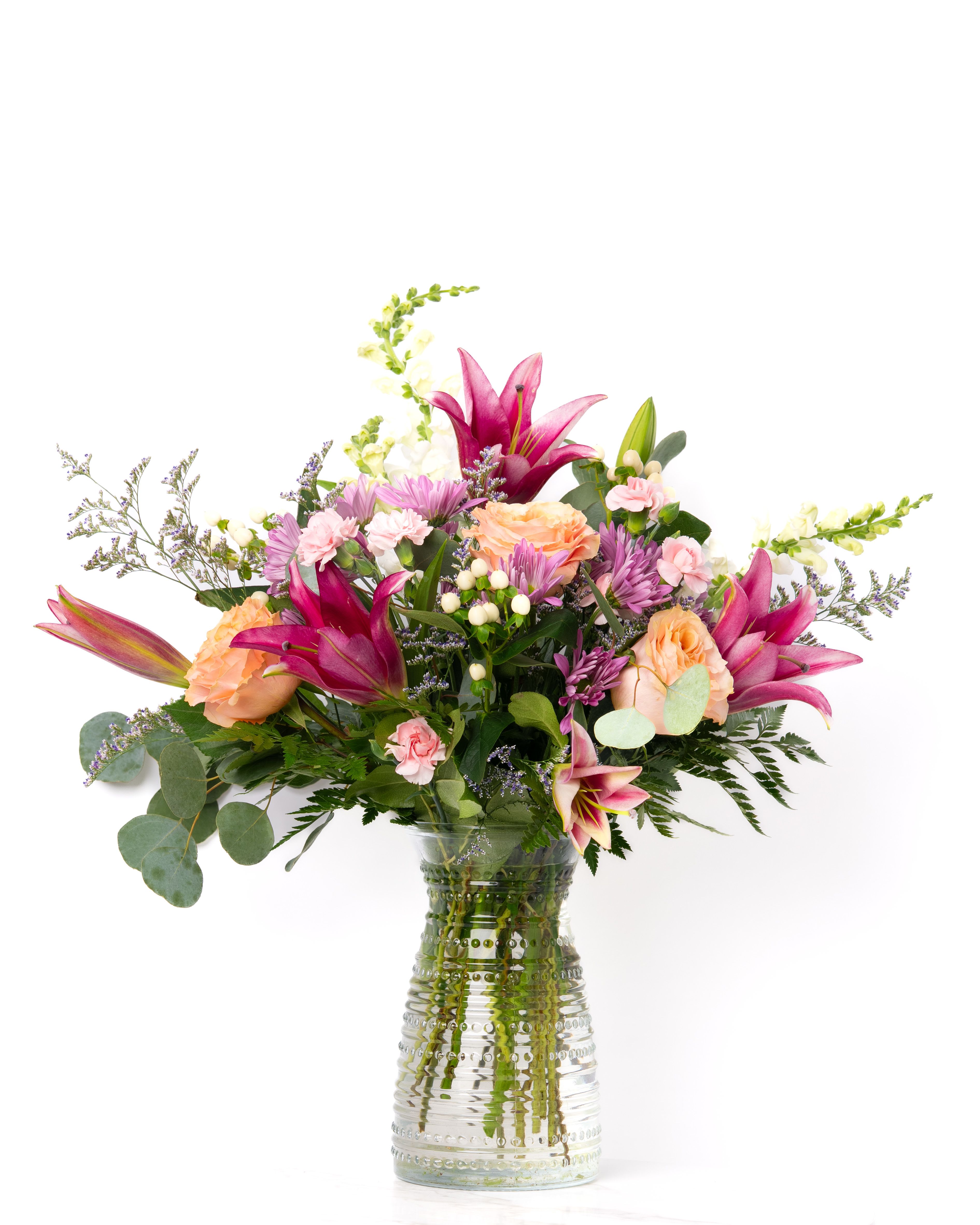 Mixed bouquet of pink lilies, peach roses, and pastel blooms in a clear textured glass vase