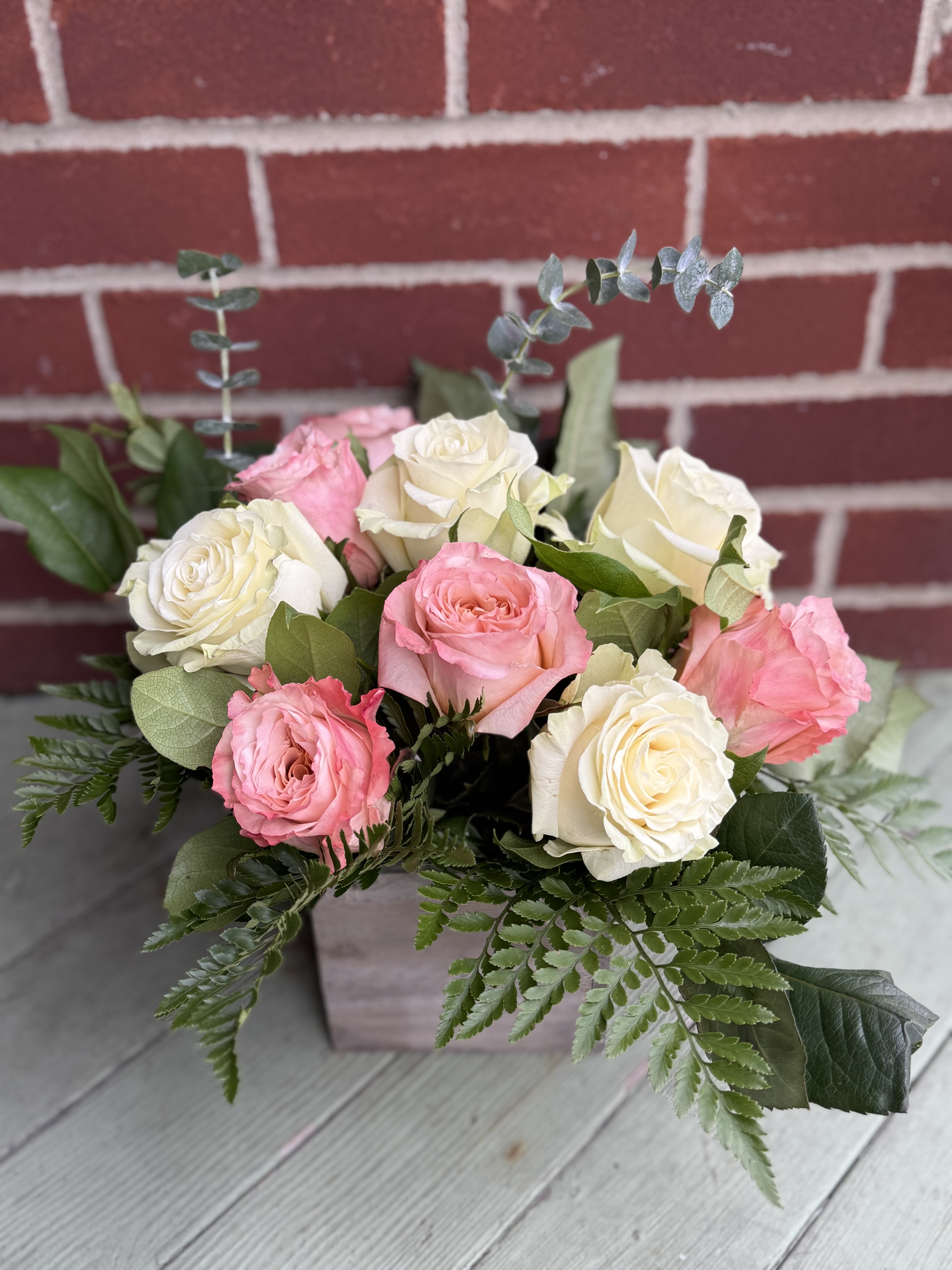 Bouquet of pink and white roses with greenery in a square container