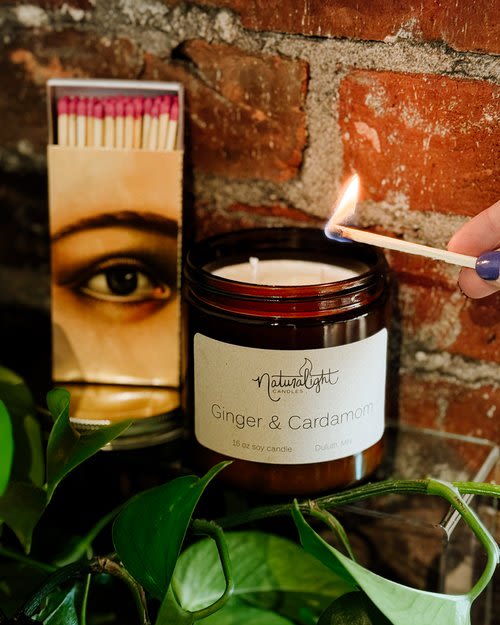 Amber jar ginger and cardamom candle being lit with a match beside a matchbox.