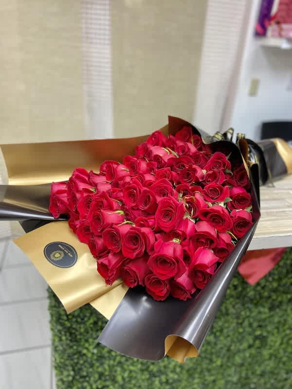 Large bouquet of tightly clustered red roses wrapped in glossy black and gold paper