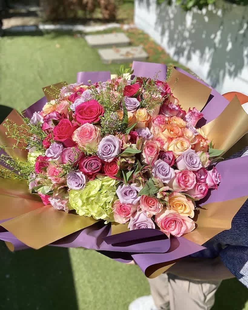 Large hand-tied bouquet of pink, lavender, and peach roses wrapped in purple and gold paper