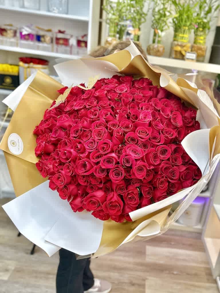 Large bouquet of hot pink roses wrapped in white and gold paper in a flower shop