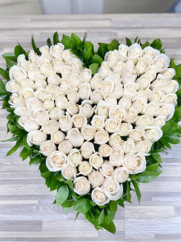 Heart-shaped arrangement of white roses edged with bright green foliage