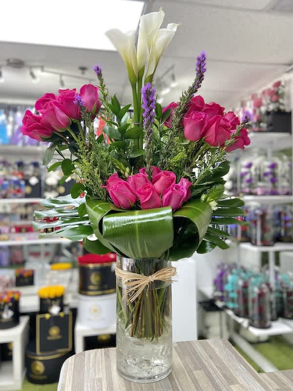 Tall arrangement of hot pink roses and white calla lilies in a clear glass vase with a collar of broad green leaves