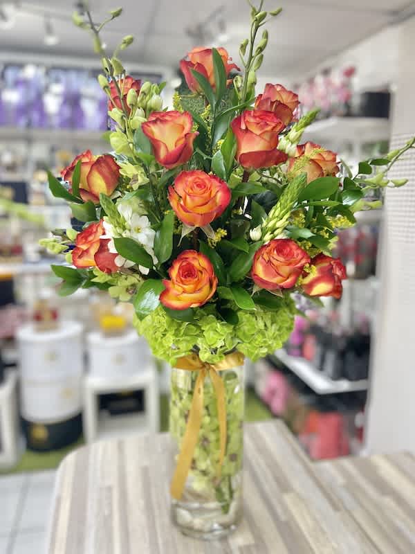Tall arrangement of orange and yellow roses with green hydrangeas in a clear glass vase