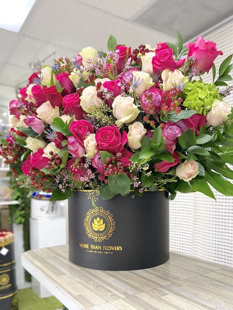 Large arrangement of hot pink and cream roses with accents in a black hat box container
