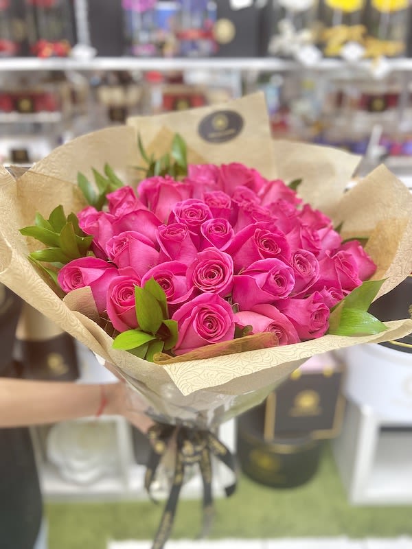 Bouquet of bright pink roses wrapped in tan patterned paper with a black ribbon tie.