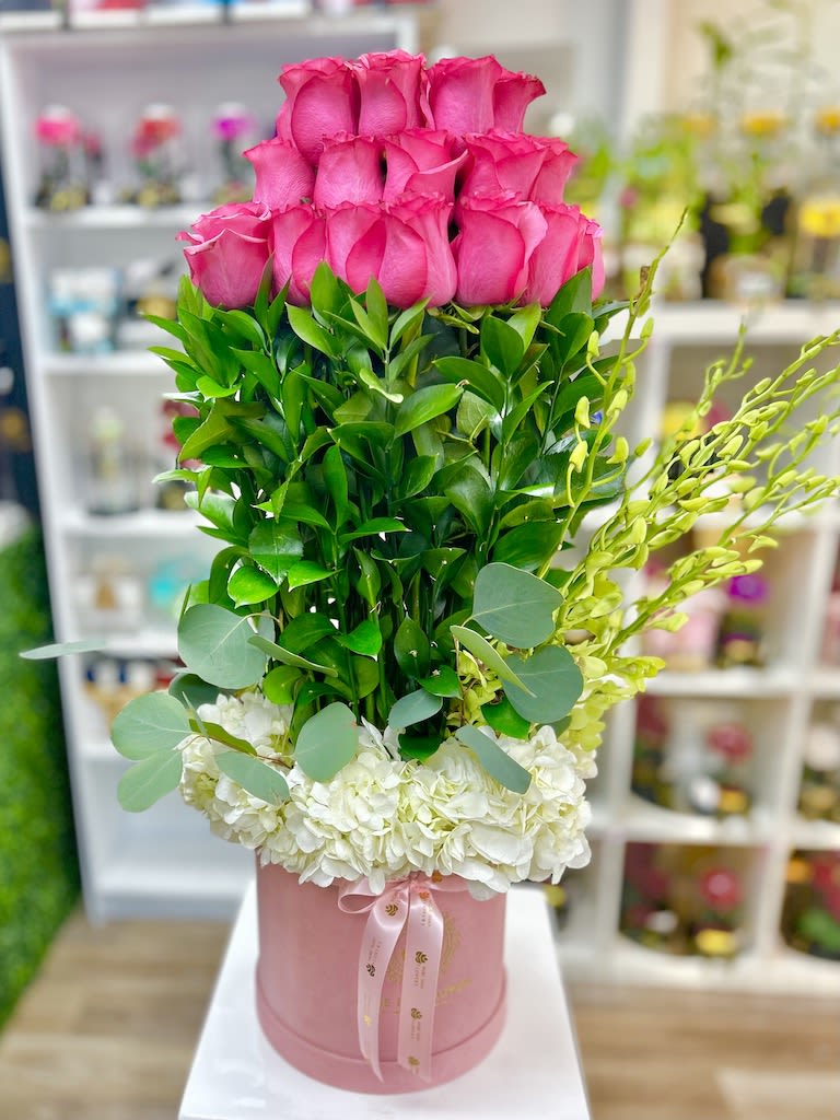 Tall arrangement of pink roses, layered greenery, and white hydrangeas in a pink hatbox.