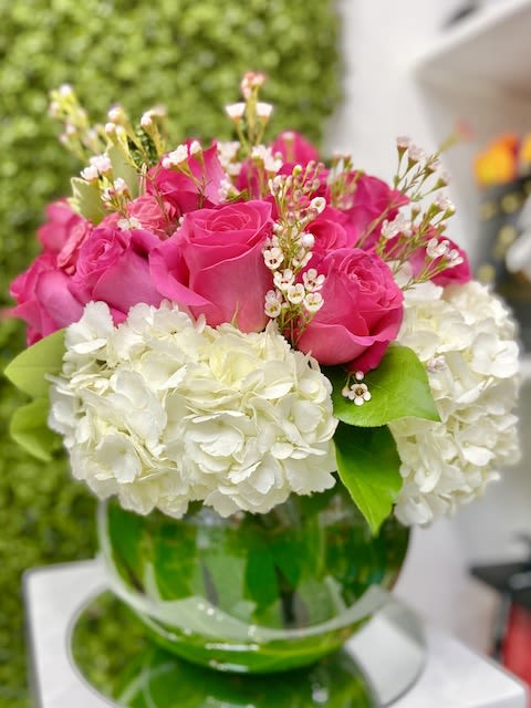 Low round arrangement of hot pink roses and white hydrangeas in a green-accented glass bowl vase