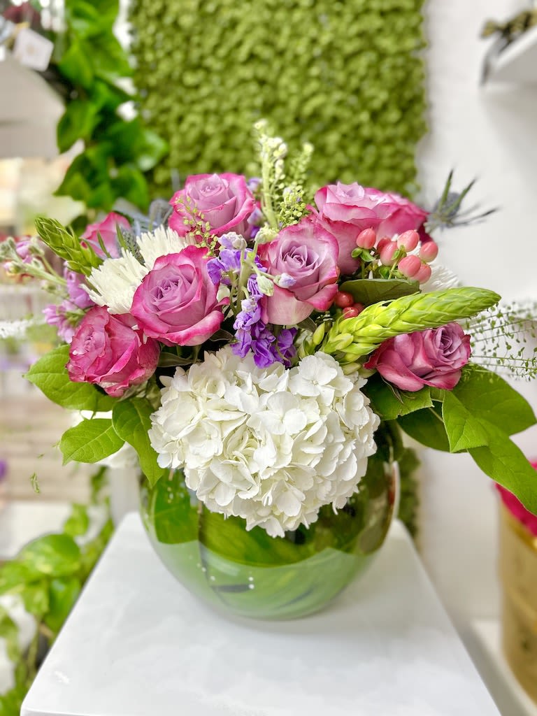 Low glass vase of pink roses and mixed blooms arranged above white hydrangeas