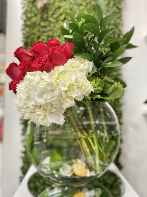 Asymmetrical arrangement of red roses and white hydrangeas in a round clear glass bowl vase