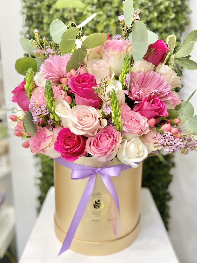 Pink and white roses with pink gerbera daisies arranged in a gold hatbox with a lavender ribbon