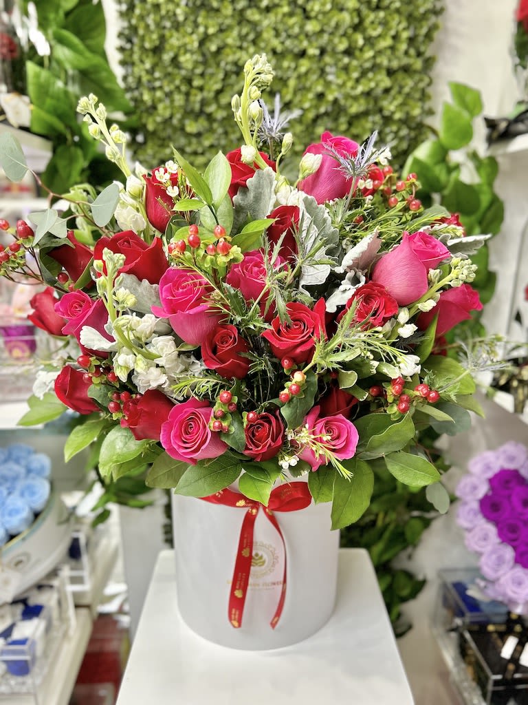 Large arrangement of red and hot pink roses in a white hatbox-style container with mixed filler flowers