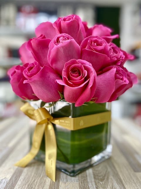 Hot pink roses arranged in a clear glass cube vase wrapped with a gold ribbon