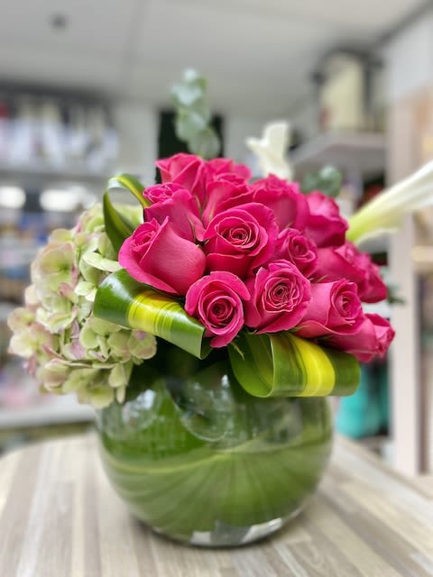 Low glass vase of hot pink roses with pale green hydrangeas and looped green leaves.