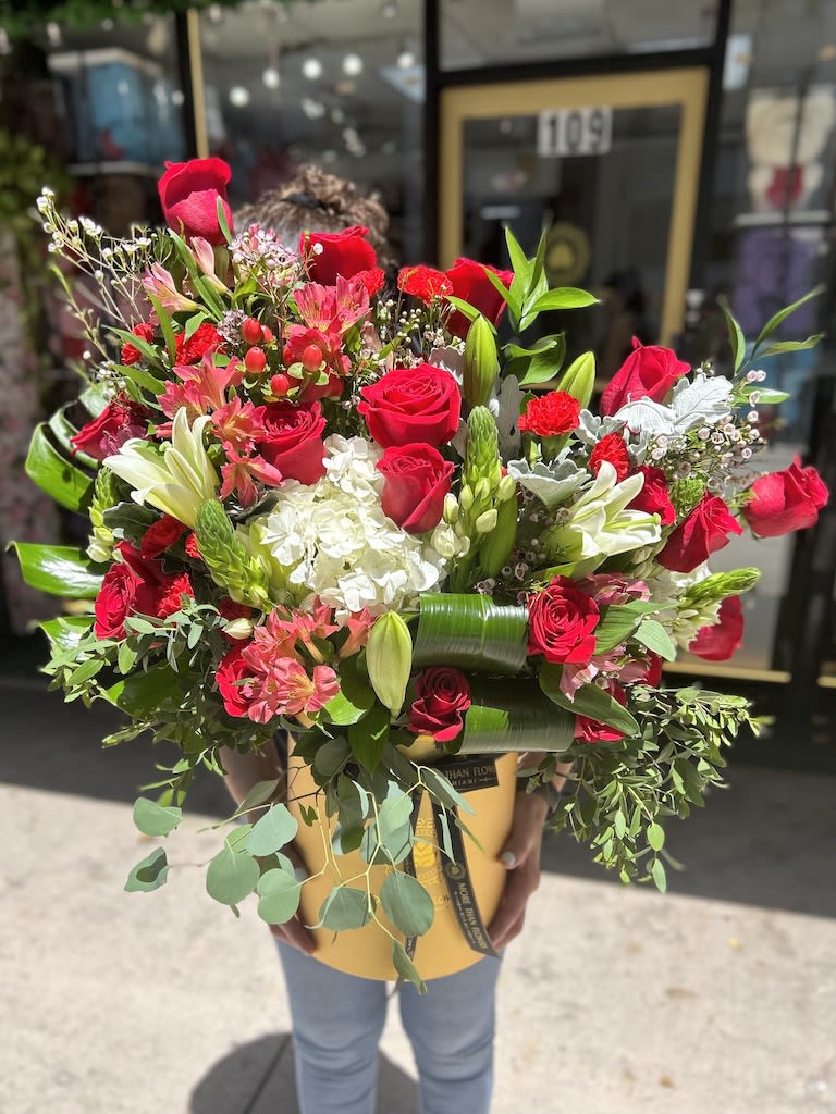 Large arrangement of red roses, lilies, and white hydrangeas in a yellow hatbox-style container