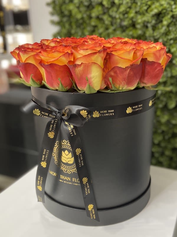 Round black hatbox filled with orange and yellow roses and tied with a black ribbon.