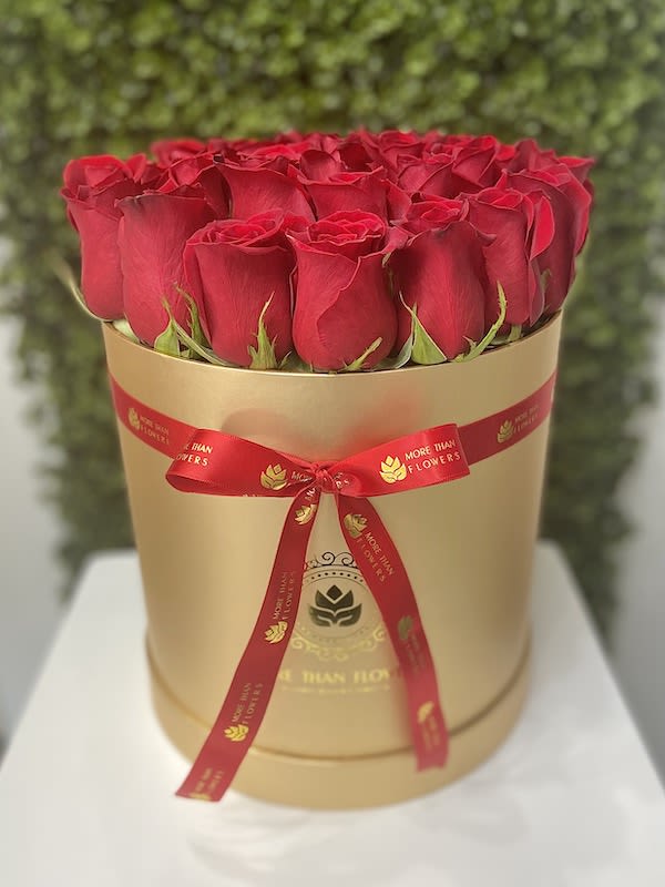 Round box of tightly packed red roses in a gold hatbox with a red ribbon bow