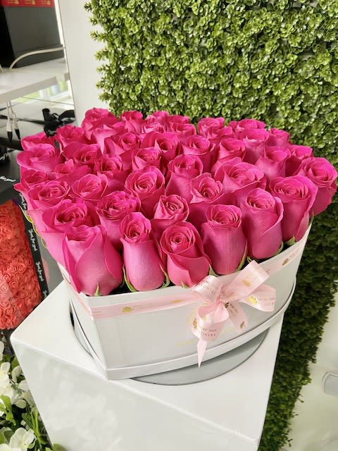 Round white hatbox filled with tightly packed bright pink roses and a pink ribbon bow